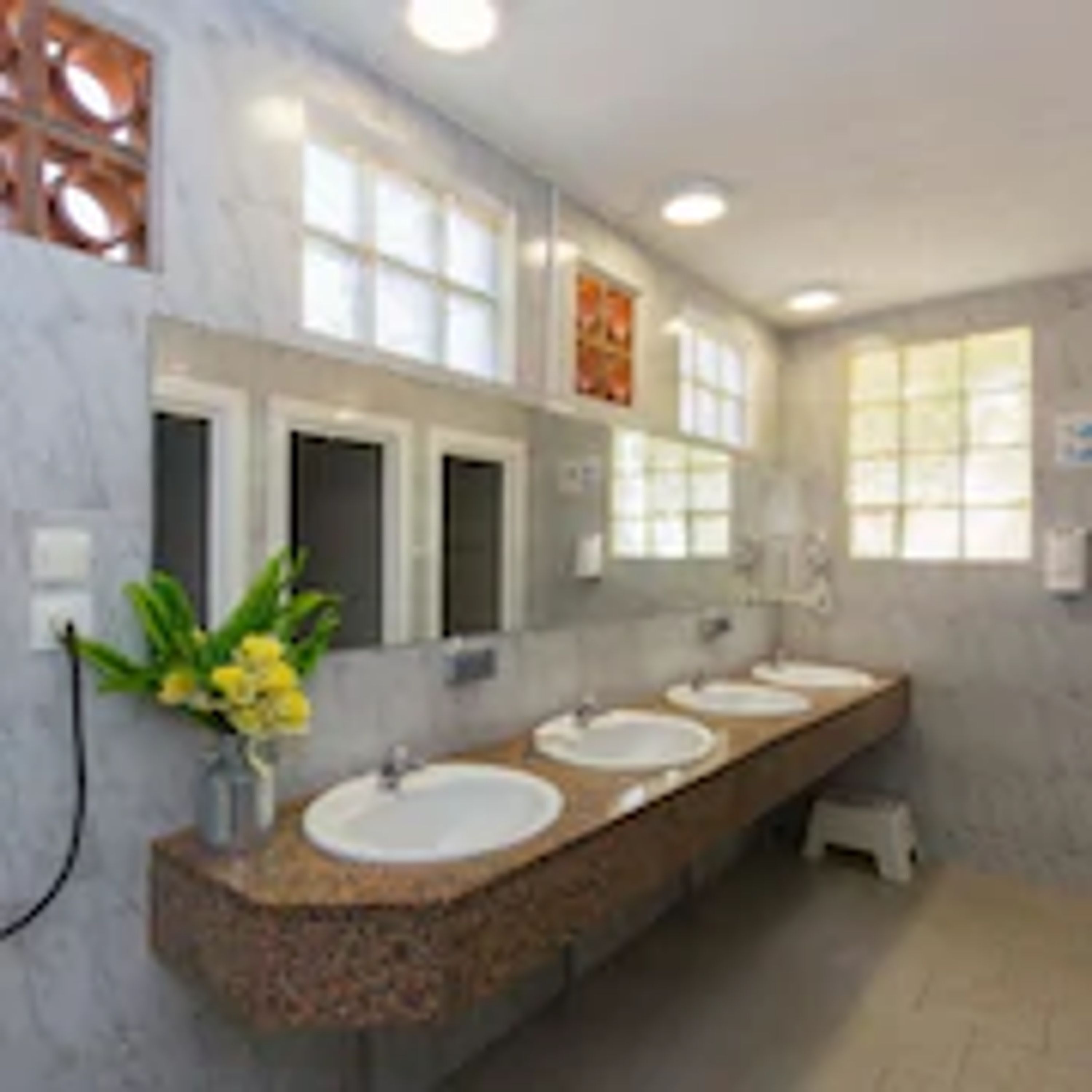 A long bathroom with three sinks, a mirror, and a window.