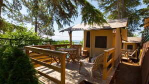 A wooden deck with outdoor seating, including tables and chairs, overlooking a body of water. - Camping El Far (Calella)