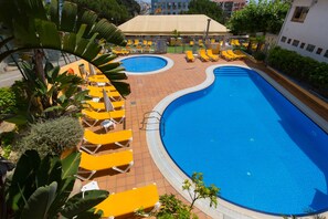 A swimming pool with yellow lounge chairs and a covered area.
