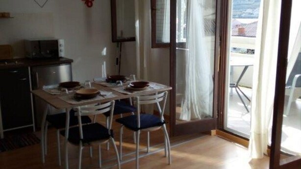 A dining area with a table and chairs, a kitchenette, and a sliding glass door leading to a balcony. - Apartment Jasenka (Pag)