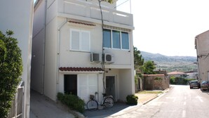 A two-story building with a bicycle parked outside, a garage door, and a view of the hills in the background. - Apartment Jasenka (Pag)