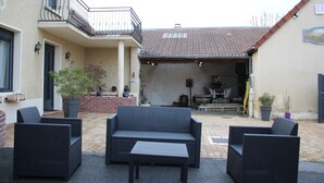 An outdoor patio area with wicker furniture, a brick wall, and a balcony. - La Part Des Anges (Mardeuil)