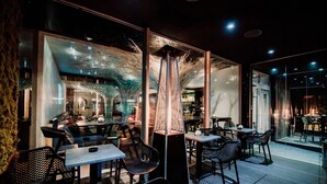 An indoor dining area with tables and chairs, a central decorative structure, and a glass wall with reflections. - BOUTIQUE HOTEL11 with rooftop SPA (Nitra)