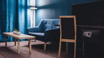 Una habitación con una pared azul oscuro, un sillón azul, una mesa de madera con dos jarrones blancos y un mueble bajo para televisión negro.