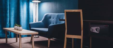 A room with a dark blue wall, a blue armchair, a wooden table with two white vases, and a black TV stand.