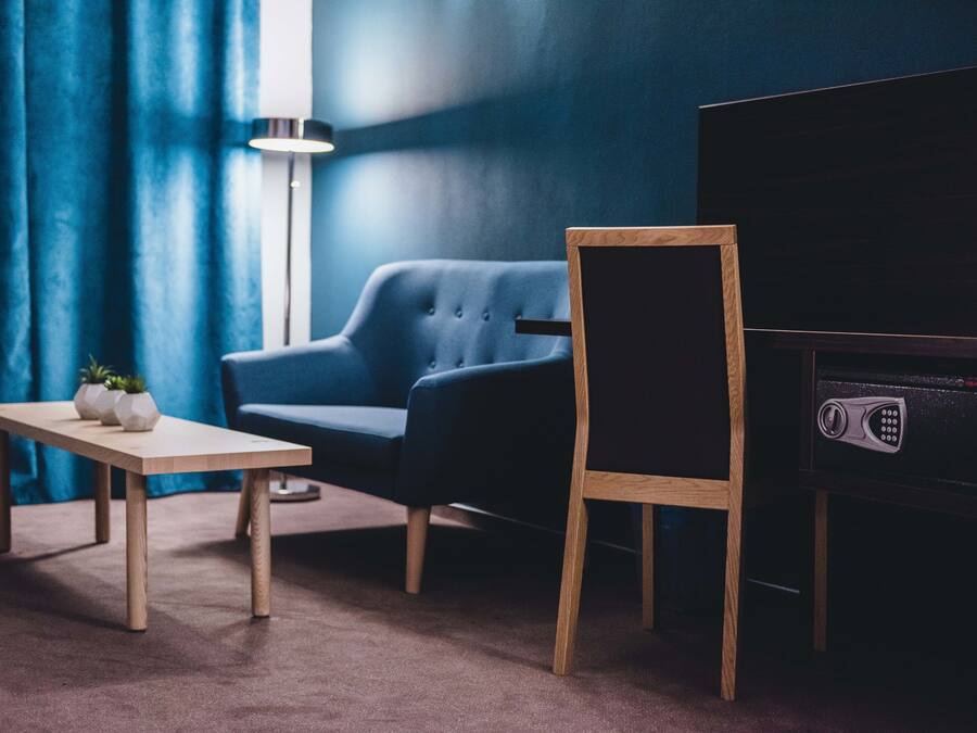 Una habitación con una pared azul oscuro, un sillón azul, una mesa de madera con dos jarrones blancos y un mueble bajo para televisión negro.