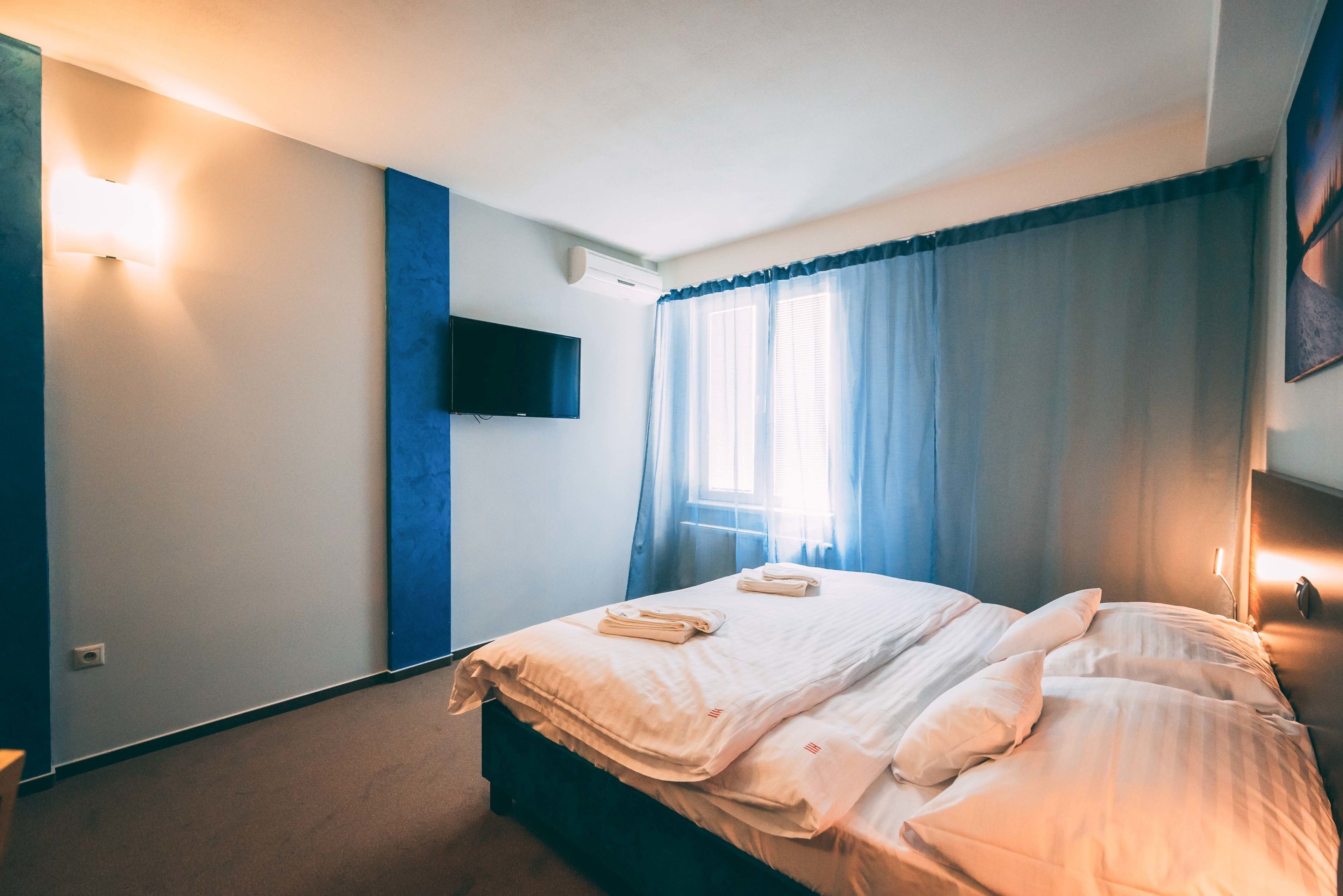 Ein Hotelzimmer mit einem Bett, einem flachbildfernseher an der Wand und einem Fenster mit Vorhängen.