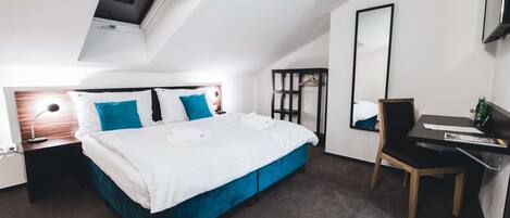 A modern hotel room with a large bed, a desk, a chair, a mirror, and a skylight.