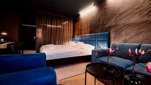 A modern hotel room with a large bed, a blue sofa, a small table, and a decorative vase with flowers. - BOUTIQUE HOTEL11 with rooftop SPA (Nitra)