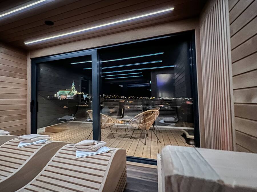 Un área de spa moderna con suelo de madera, sillones de descanso y una puerta de cristal que da a vistas de la ciudad.