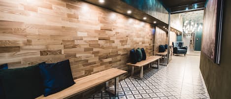 A modern interior with wooden benches and a patterned floor, featuring a seating area and a view into another room.