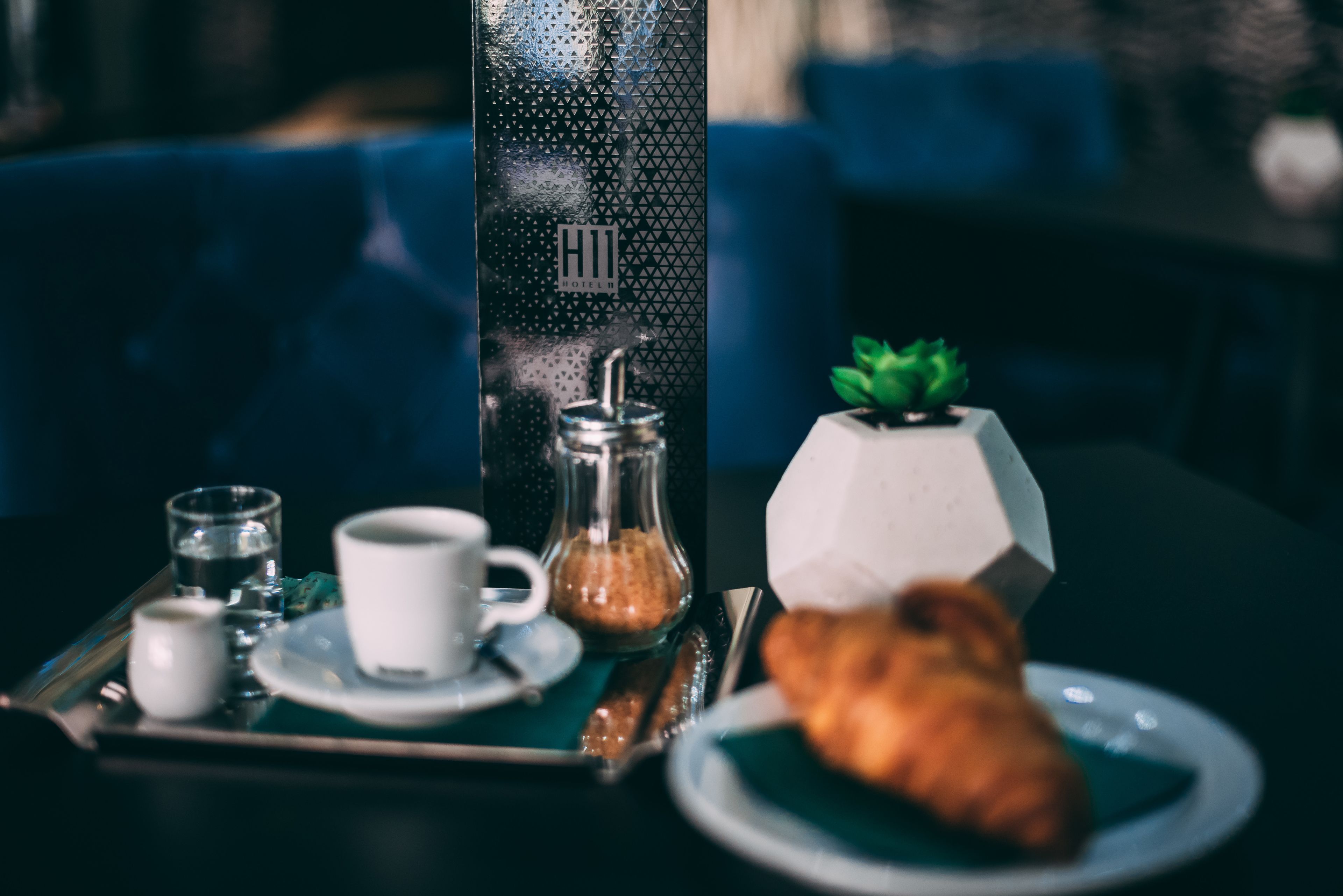Un plateau de petit-déjeuner avec un croissant, une tasse de café et un sucrier, posé sur une table.