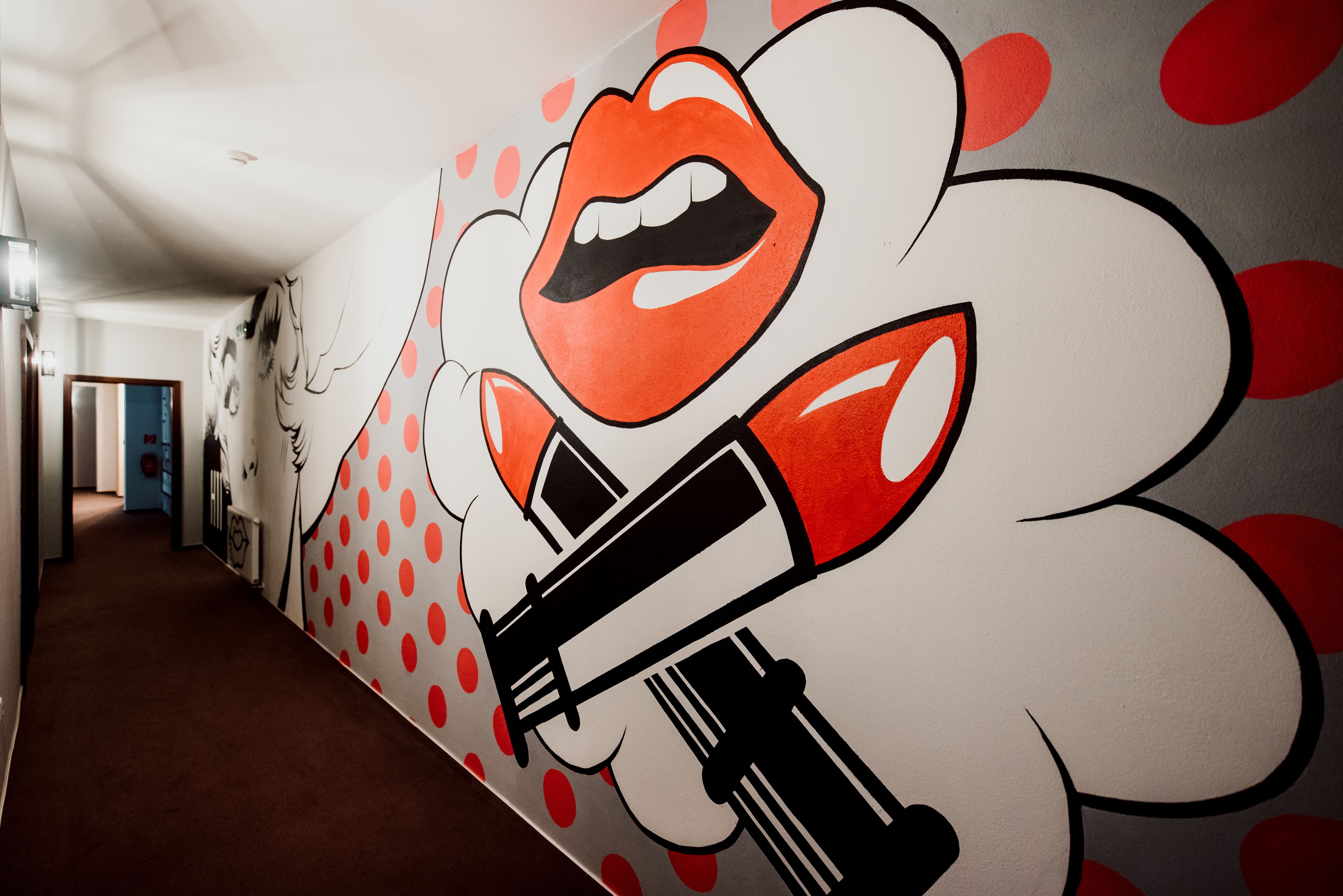 Un pasillo con un mural que presenta un rostro estilizado y labial.
