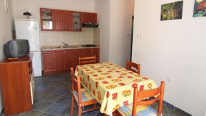 A compact kitchen with wooden cabinets, a refrigerator, a stove, and a dining table with chairs.
