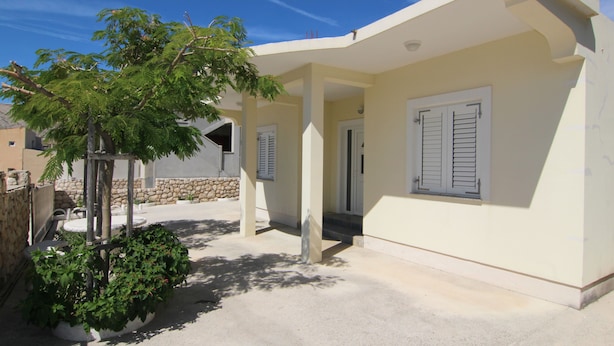 A modern building with a covered patio area, stone walls, and a tree providing shade.