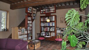 A cozy library with wooden bookshelves, a purple sofa, and a table with books. - Les Jardins de Beauve (Héricourt-sur-Thérain)