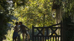 A wooden gate with a cross design, a bicycle, and a person riding it. - Les Jardins de Beauve (Héricourt-sur-Thérain)