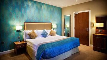 A hotel room with a large bed, two bedside tables with lamps, a wooden wardrobe, and a teal patterned wall.