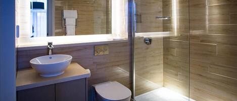 Een moderne badkamer met een grote spiegel, een wastafel op standaard, een toilet en een douche met glazen wanden.