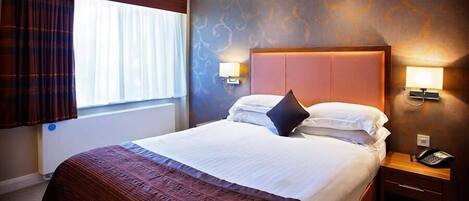 A hotel room with a large bed, a nightstand with a phone, and a window with curtains.