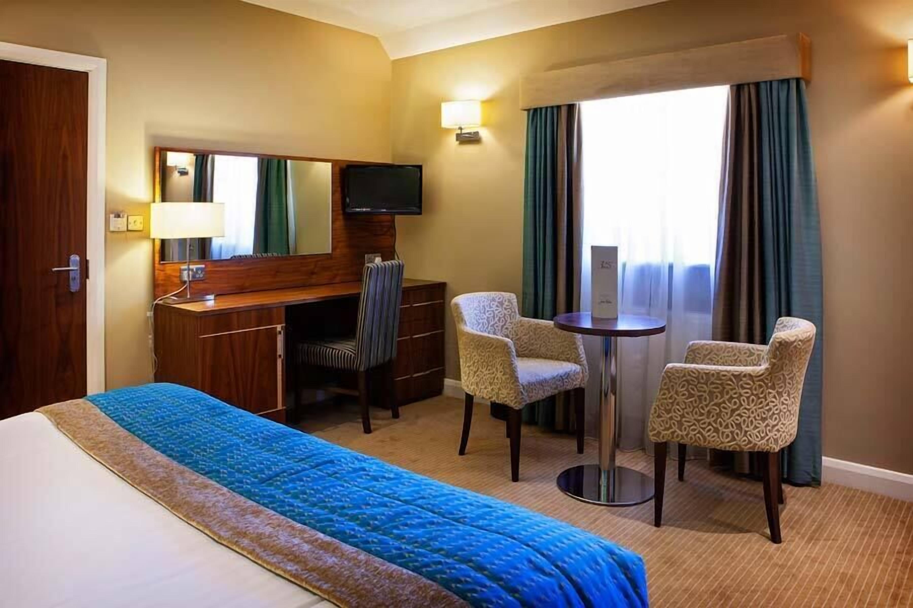 A hotel room with a bed, a desk, a chair, a television, and a window with curtains.