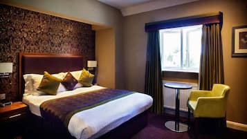 A hotel room with a large bed, a small round table, a yellow armchair, and a window with curtains.