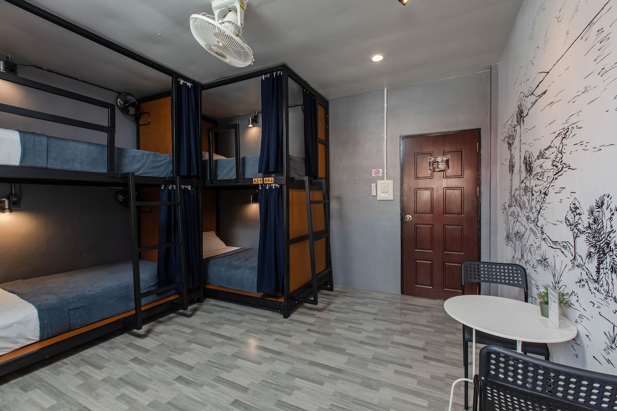Un dormitorio con literas, un ventilador, una mesa y una puerta.