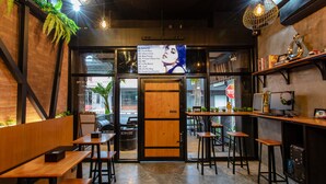 Un interior de restaurante con mesas y sillas de madera, un tablero de menú y una computadora sobre un mostrador.