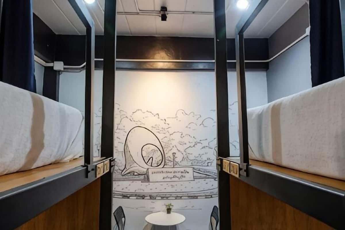 Un compartimento de tren con literas, un mural, una mesita y sillas.