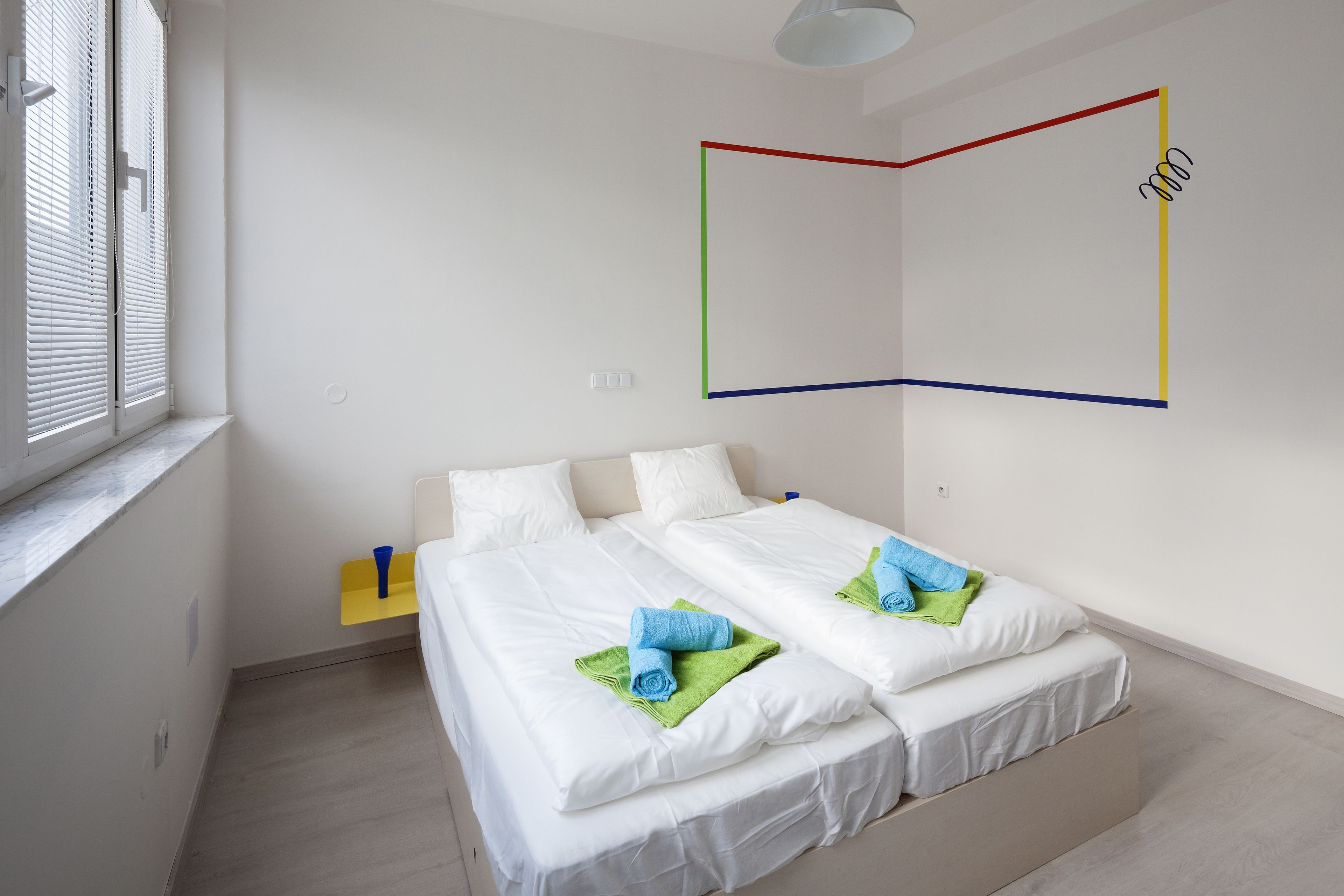 A modern hotel room with two beds, a small bedside table, and a window with blinds.