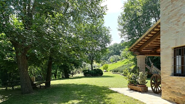 Un jardín cuidado con un banco de madera, un muro de piedra y un edificio rústico con una gran rueda de madera.