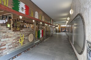 Un couloir avec un mur de briques sur la gauche et un mur de verre sur la droite, qui mène à un restaurant appelé « El Pueblo Mexican Steak House ».