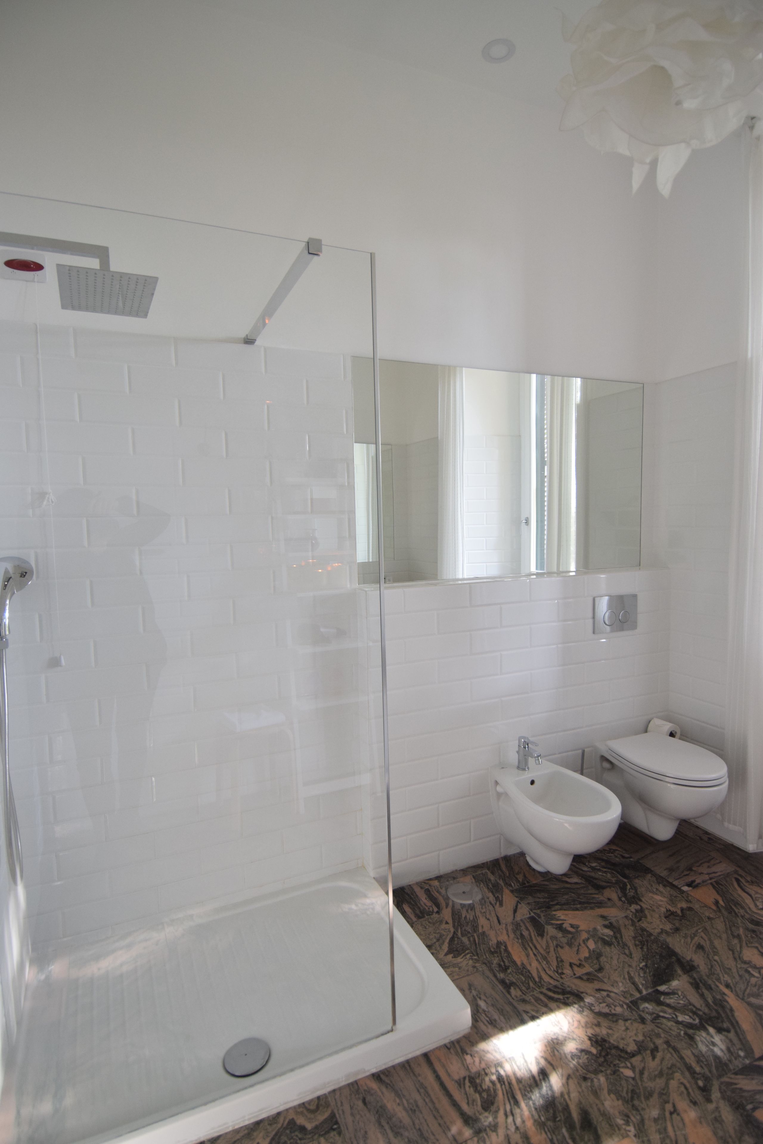 A bathroom with a glass-enclosed shower, white tiled walls, a marble floor, and a bidet.