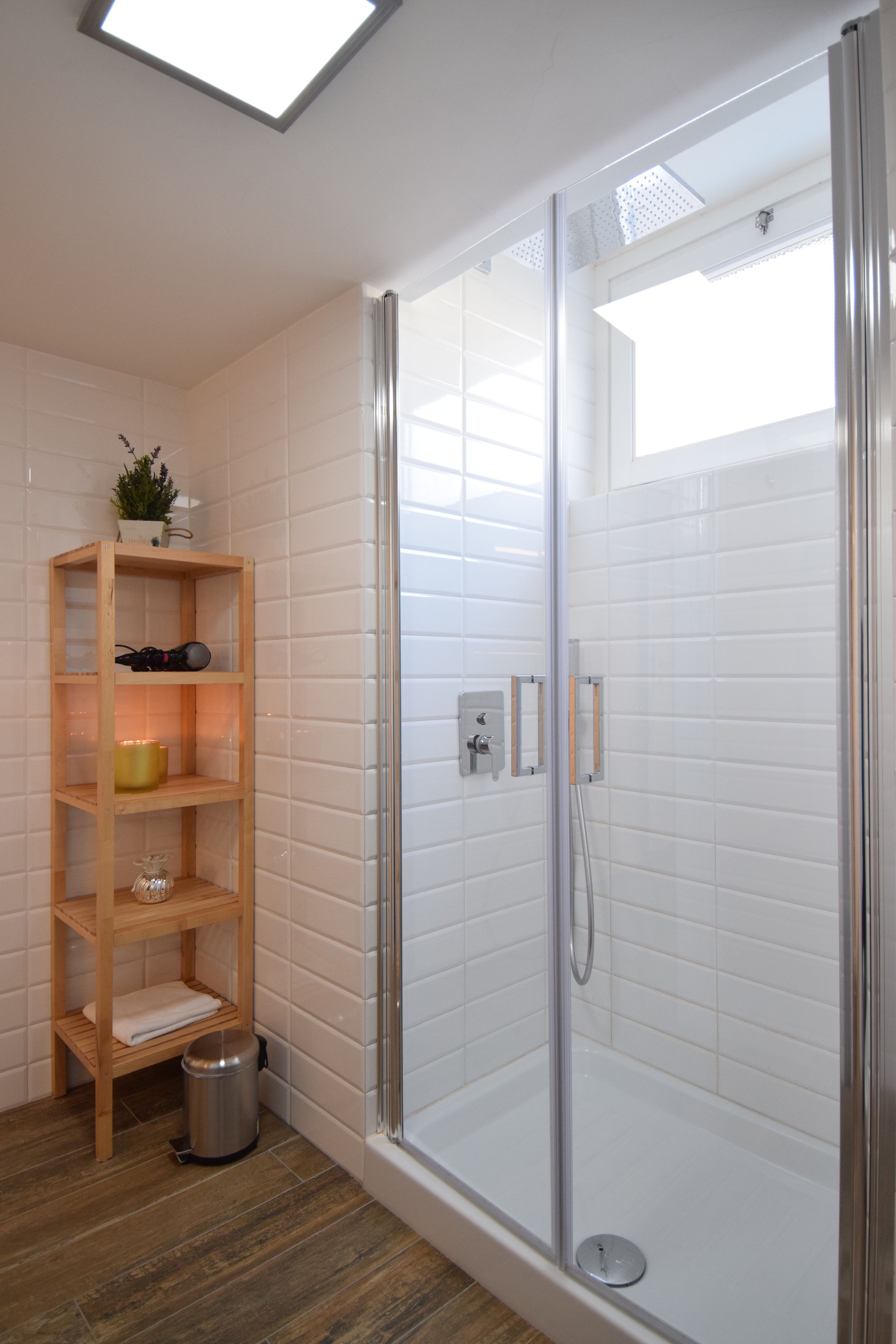 Un espace douche doté d’une porte en verre, d’étagères en bois et d’une poubelle.