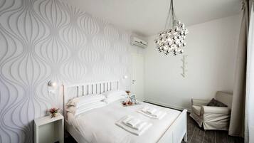 Une chambre d’hôtel moderne avec un grand lit, une tête de lit blanche, un mur décoratif, un lustre et un petit coin salon.