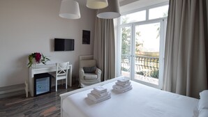 Quarto de hotel com cama, escrivaninha, cadeira, televisão e janela com cortinas.