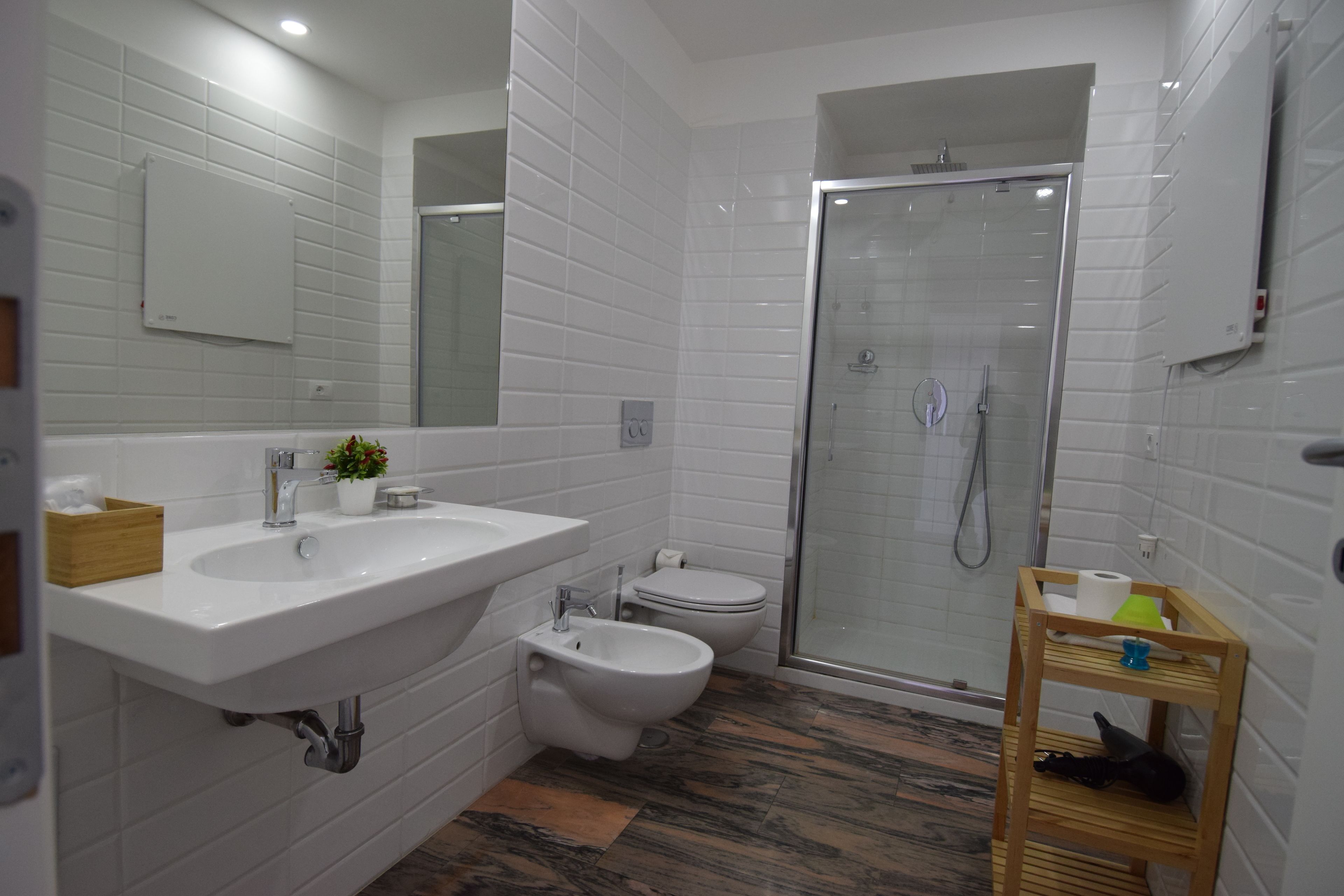 A modern bathroom with a white sink, bidet, and glass-enclosed shower.