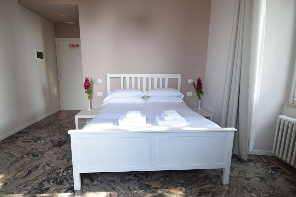 Un lit bien fait, avec du linge de lit et des serviettes blancs, une tête de lit blanche et deux tables de chevet avec des lampes.