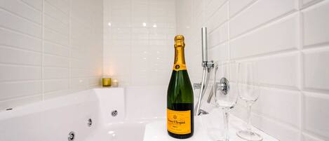 A bathroom with a white bathtub, a bottle of champagne, and two wine glasses on the sink.