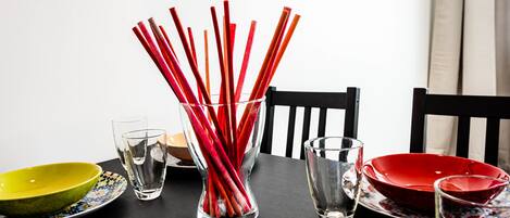 A dining table with a clear glass vase containing red straws, a yellow bowl, and a red bowl.