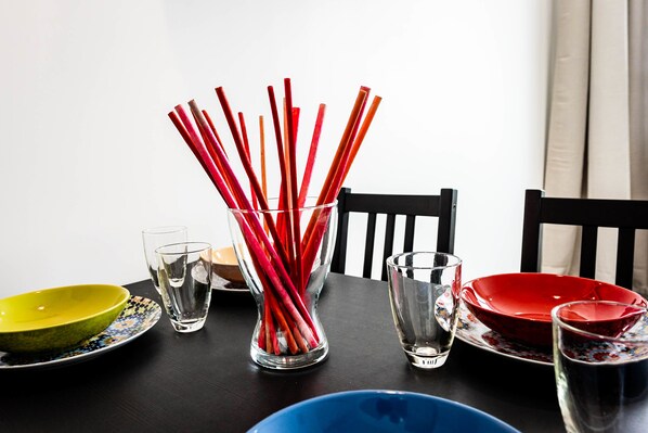 A dining table with a clear glass vase containing red straws, a yellow bowl, and a red bowl.