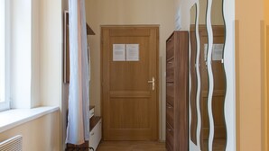 A hallway with a wooden door, a radiator, a window with a curtain, and a wall-mounted mirror. - Premier Apartment near Museum (Prague)