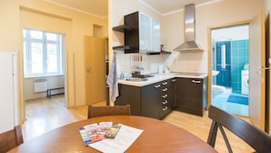A modern kitchen with a dining table, cabinets, and a view into the bathroom. - Premier Apartment near Museum (Prague)