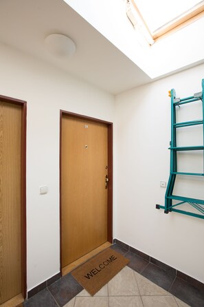 A hallway with a wooden door marked with the number 38, a welcome mat, and a green metal rack against the wall. - Premier Apartment Vysehrad (Prague)