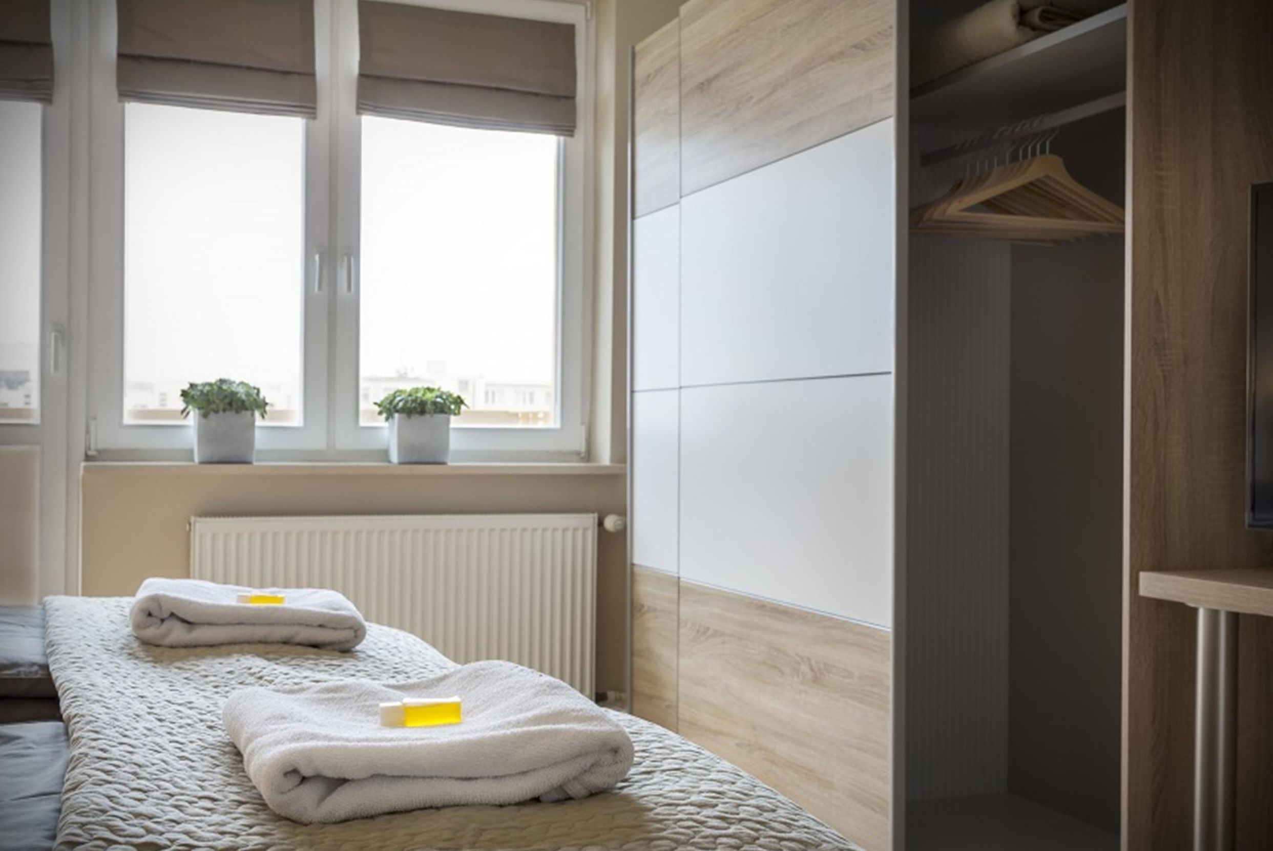 Un dormitorio con cama, ventana con plantas, radiador y armario.