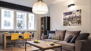 A modern living room with a sofa, a dining table with chairs, a pendant light, and a cityscape painting on the wall.