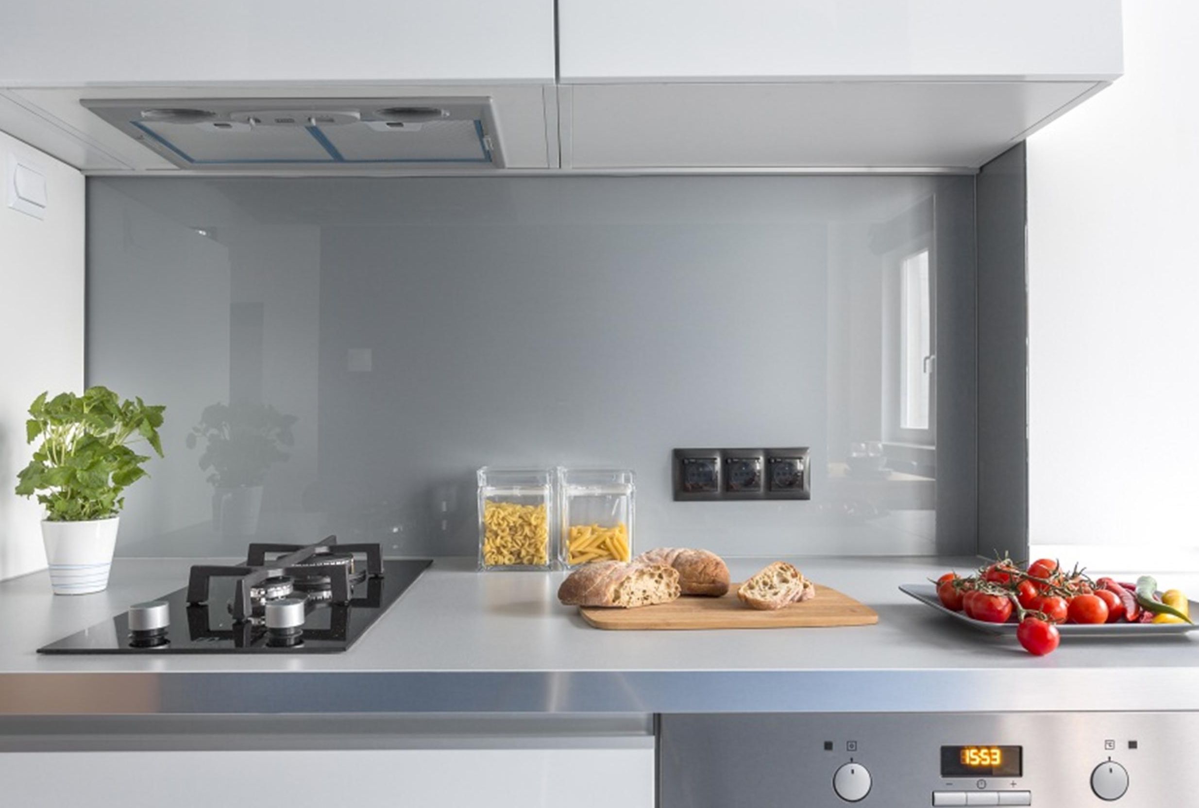 A modern kitchen with a built-in stove, two glass jars of pasta, a cutting board with bread, and a plate of tomatoes.