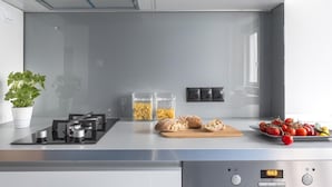 A modern kitchen with a built-in stove, two glass jars of pasta, a cutting board with bread, and a plate of tomatoes.