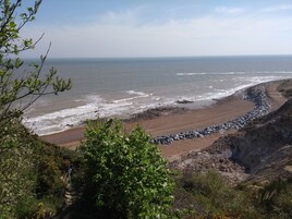 A coastal landscape with a rocky beach, vegetation, and a clear view of the ocean.