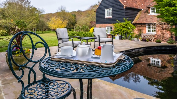 A garden setting with a table set for tea, chairs, and a house in the background. - Stream House Luxury B&B (Hastings)